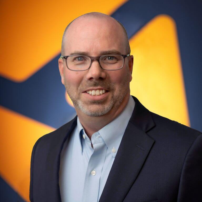 A man with glasses in a blue suit jacket, staring at the camera