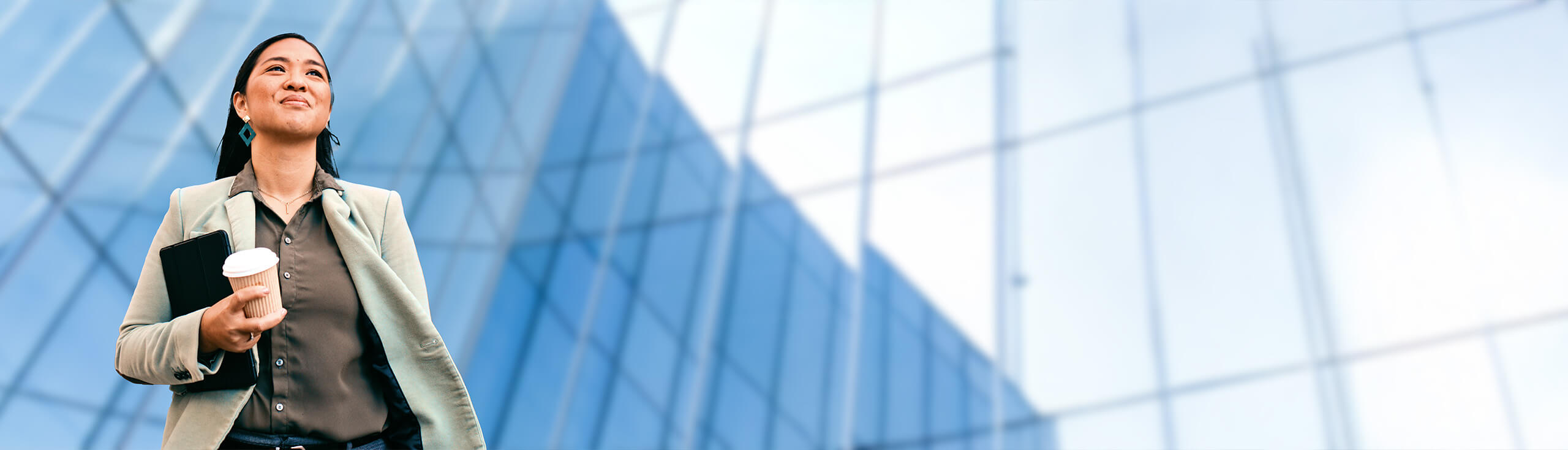 A woman standing outside a tall glass building, smiling.