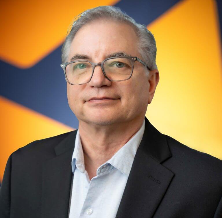 A man with gray hair and glasses ina black suit coat