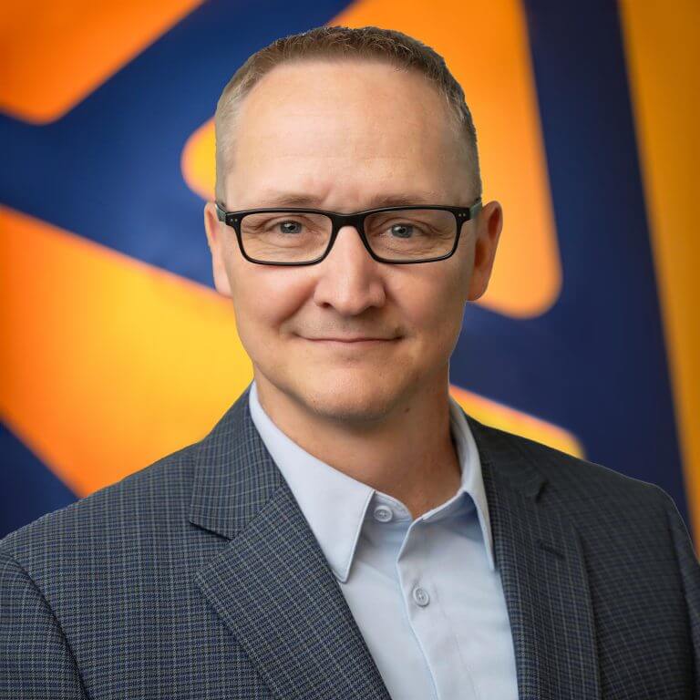 A man with black framed glasses looking at the camera with a plaid suitcoat